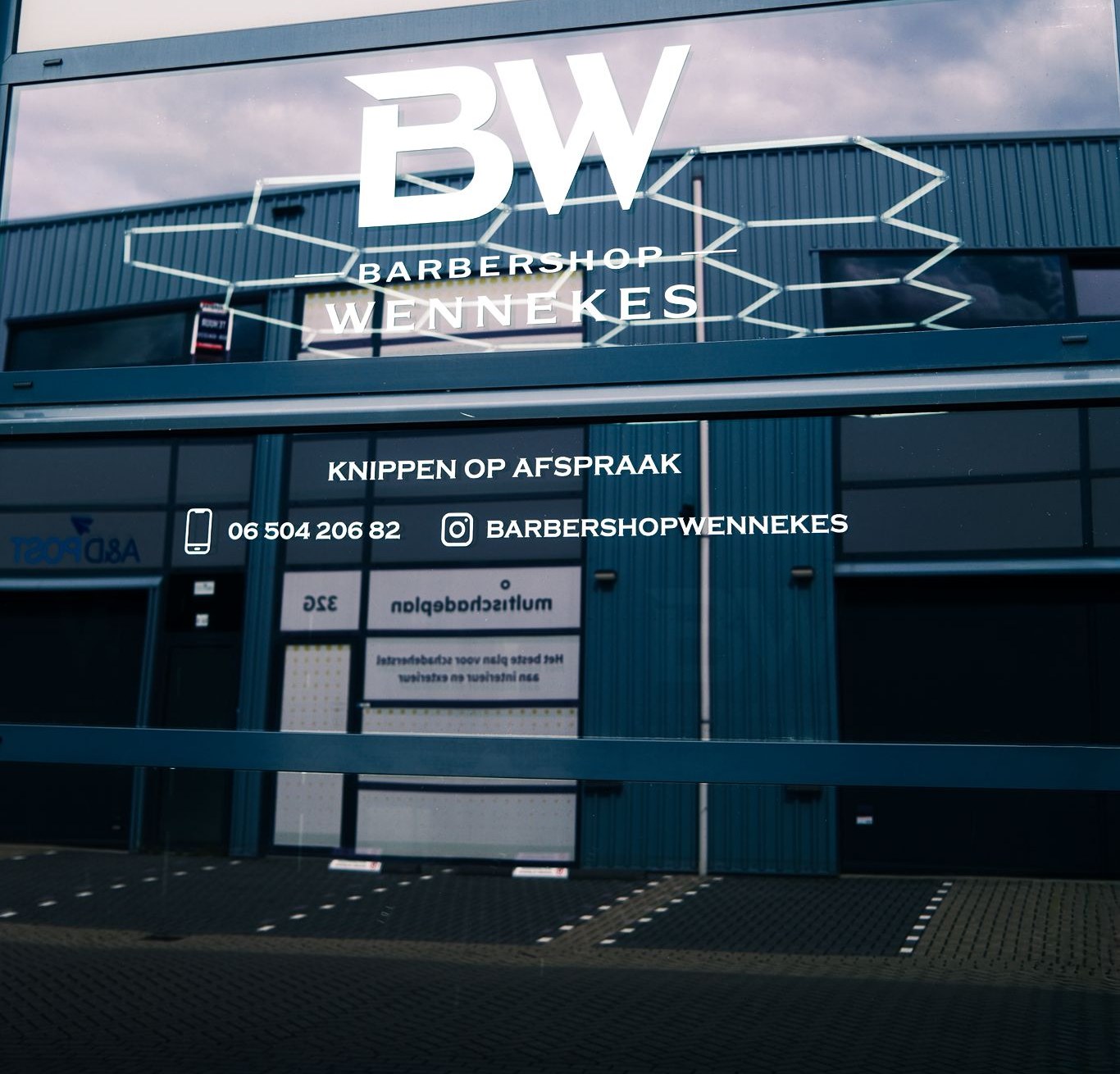 De gevel van Barbershop Wennekes aan de Lange Schaft: het BW-logo op het glas, met Knippen op afspraak, het telefoonnummer en de Instagramnaam